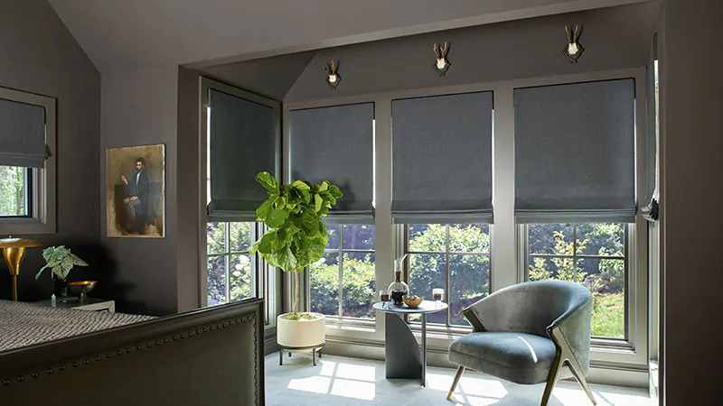 A bedroom with warm dark grey walls features tall windows with Flat Roman Shades made of Wool Blend in Charcoal
