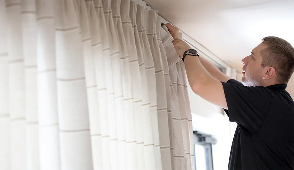 A professional installer shows how to install curtain rods and hang drapery on a track system with hooks