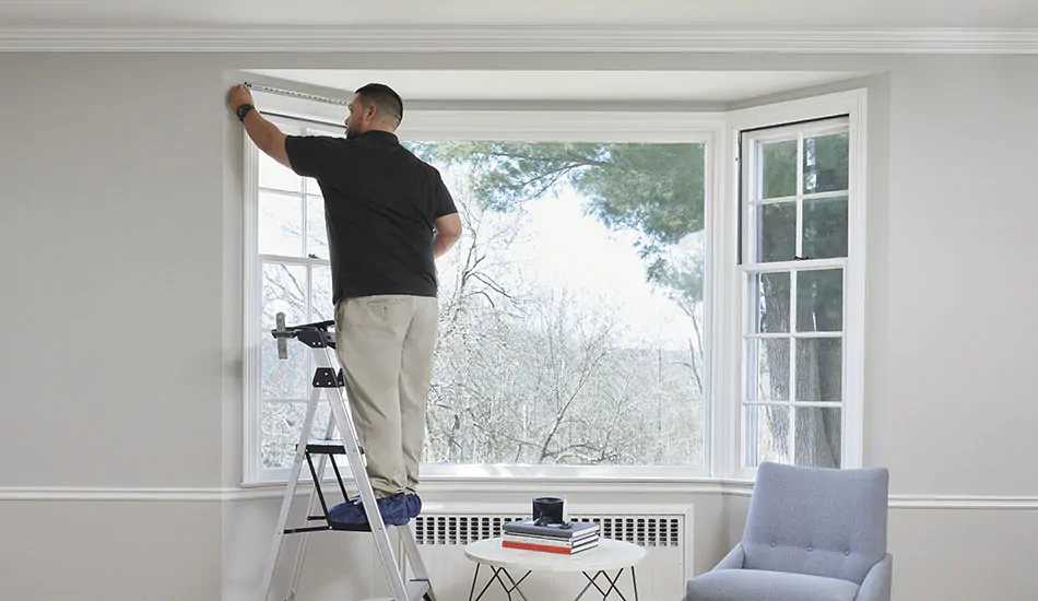 A professional from The Shade Store measures a bay window in preparation for the installation of bay window curtains