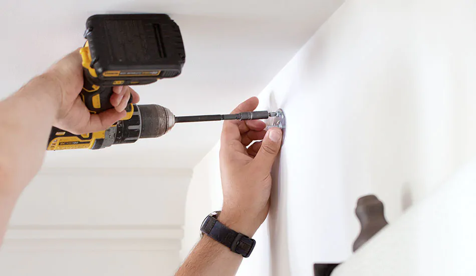 An install professional uses a drill to fasten the brackets as part of the steps for how to install drapes