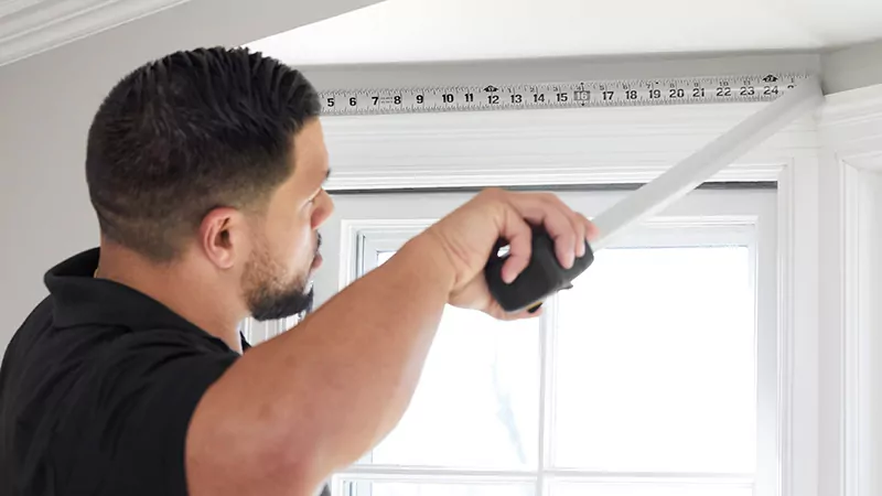 A professional window treatment installer measuring one window with a measuring tape for a bay window treatment application