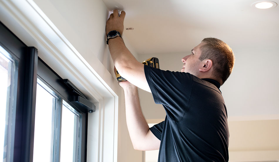 A professional window treatment installer marks the bracket placement for drapery above a window with black mullions