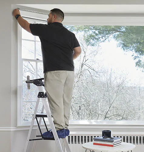 A professional window treatment installer measures a bay window before installing window treatments for bay windows
