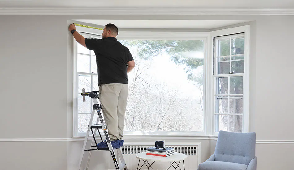 A professional measures the top of a window frame showing how to measure for curtains for a bay window