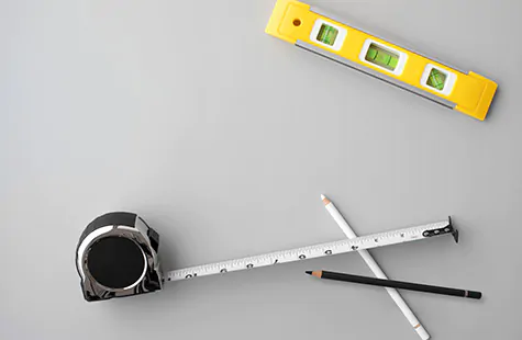 A tape measure, pencils and a level lie on a table and show the common tools needed to know how to install blinds