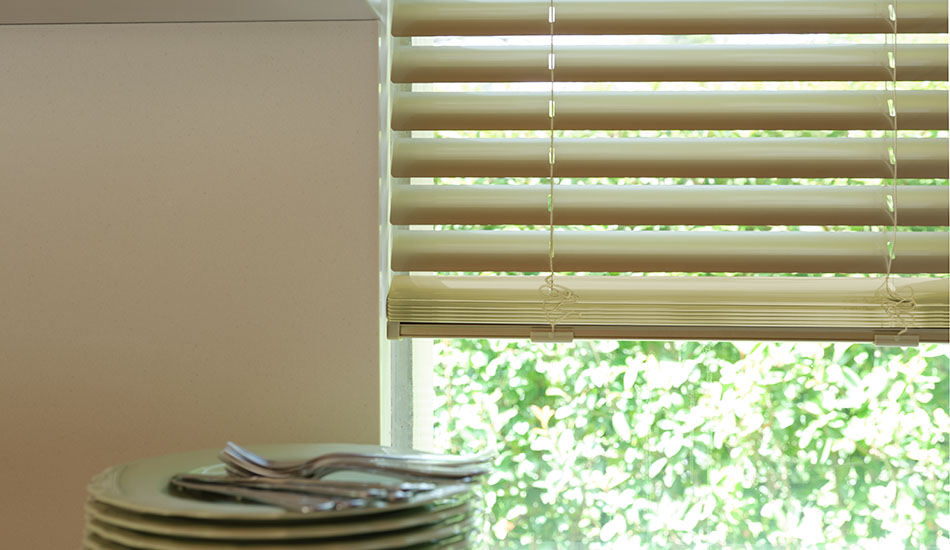 Gold champagne metal blinds used in a kitchen window next to a counter with plates are one option blinds for bay windows