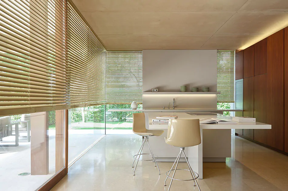A warm modern kitchen features gold metal blinds for tall windows that expand from the floor to the ceiling