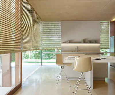 A modern kitchen features tall corner windows witih Metal Blinds made of 2-inch Champagne aluminum slats for a warm look