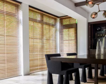 2 Inch Champagne Metal Blinds hung over floor to ceiling windows in a dining room with a large table with black chairs