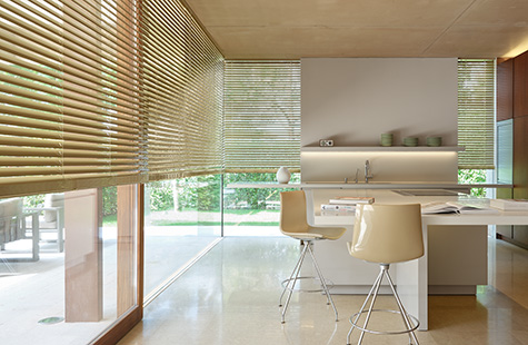 A bright, warm kitchen with tall windows has Metal Blinds made of Champagne giving the space an inviting golden hue as durable window treatments with adjustable privacy