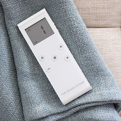 A motorization remote lays on a piece of fabric suggesting how to put blinds down with a motorization control system