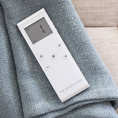 A motorization remote lays on a piece of fabric suggesting how to close blinds with a motorization control system