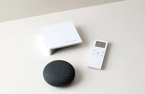 The Shade Store Wireless Link sits on a white table with a motorized window treatment remote as well as a smart home device