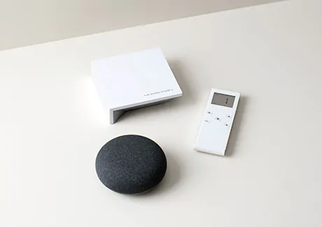The Shade Store motorization remote and wireless link sit on a white table next to a smart home device