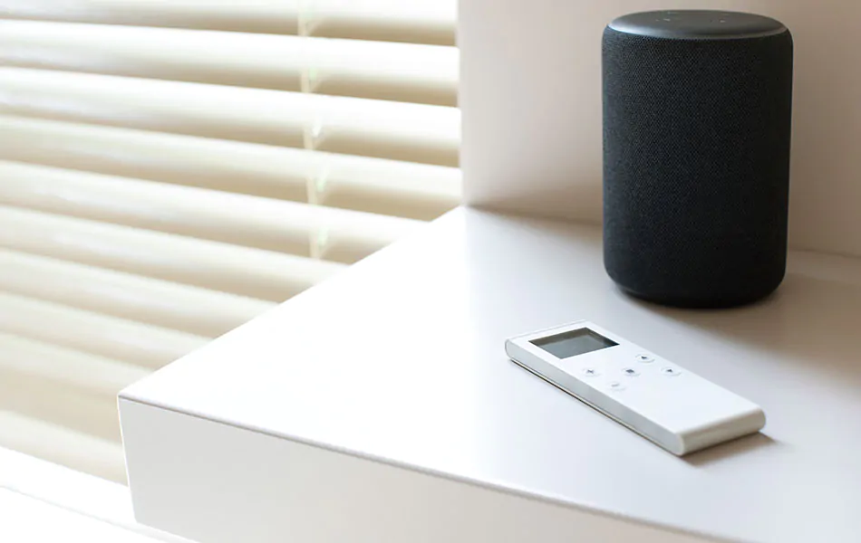 A remote for motorized Metal Blinds made of 2-inch slats in Champagne sits on a table next to the window