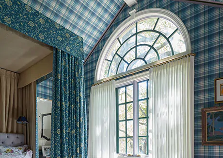 A blue patterned bedroom has curtains for arched windows made of Pinch Pleat Drapery in C.O.M. hung below the arch