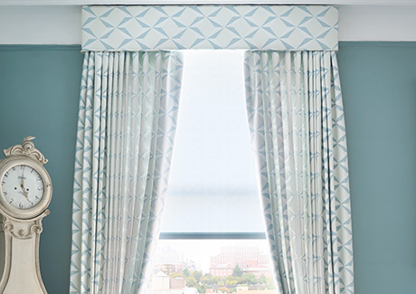 Window coverings in a cool blue room include Pinch Pleat Drapery made of Pin Wheel in Lagoon and a matching cornice