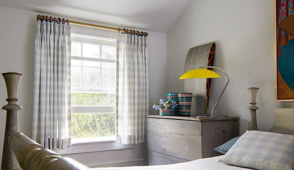 Basement window curtains made of Pinch Pleat Drapery of Emerson in Sky add a touch of pattern to a bedroom