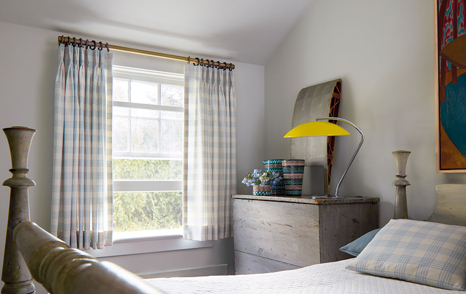 A bedroom has sill-length kids curtains made of Holland & Sherry Emerson in Sky with a matching pillow on the bed