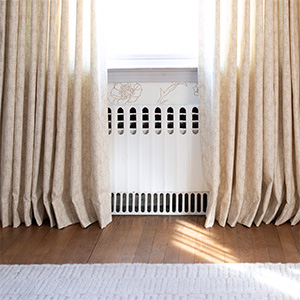 Pinch Pleat Drapery made of Nate Berkus Paloma in Sandstone kisses the warm wood floor of a bedroom with floral wallpaper