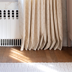 Pinch Pleat Drapery panels made of Paloma in Sandstone gently kiss the warm wood floors which helps hide uneven floors