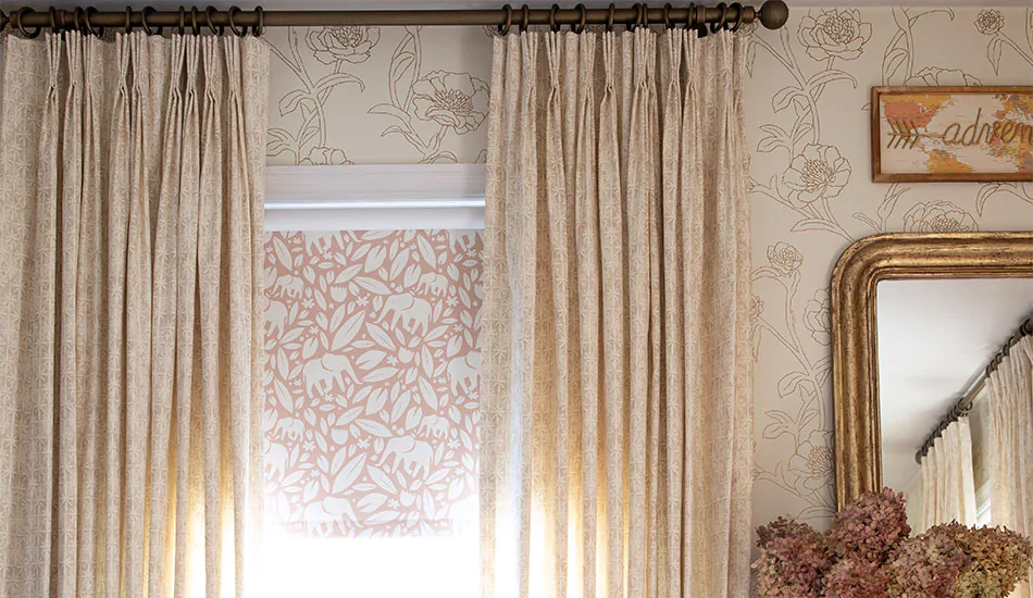 Nursery window treatments include Pinch Pleat Drapery made of Paloma in Sandstone and Blackout Roller Shades made of Eleo