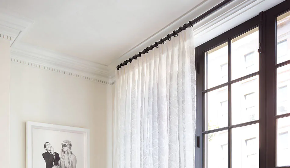 Close up shot of sheer white drapery on a black rod just below the ceiling shows how to hang curtains with crown molding