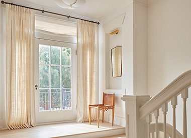 A stairwell landing has a door to the outdoors covered in drapery panels of Pinch Pleat Drapery made of Raw Silk in Glacier