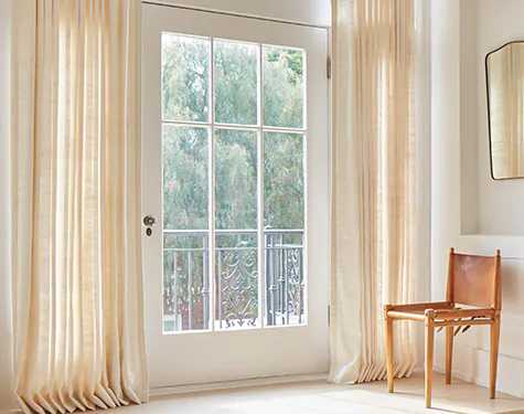 A glass door with a white frame is framed by one of the types of drapes, natural drapes made from Raw Silk in Glacier