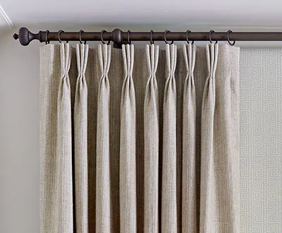 A close-up shot of reed-colored thermal curtains, specifically pinch pleat drapery, hanging along an ornate rod