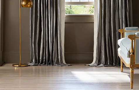 A living room with dark gray curtains and light wood floors shows how to hang curtains with a puddle length