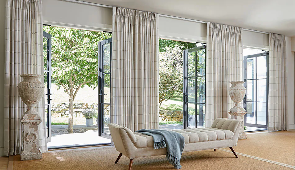 Pinch Pleat Drapery made of Sankaty Stripe in Sand are used as sunroom window treatments in a large room with big glass doors