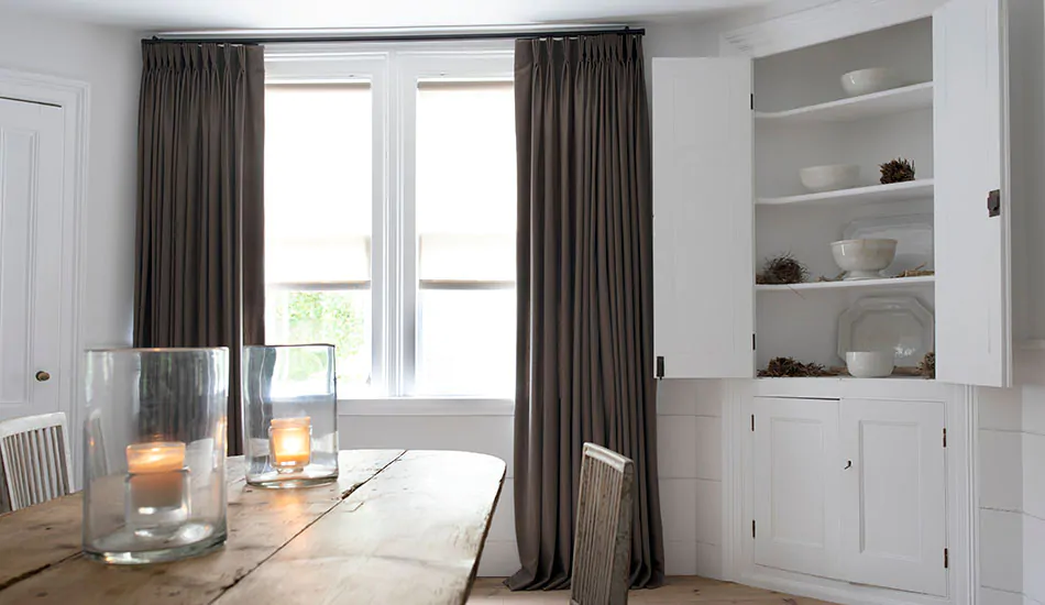 A dining room with a rustic wood table has grey curtains in the Pinch Pleat style made of Wool Flannel in Walnut