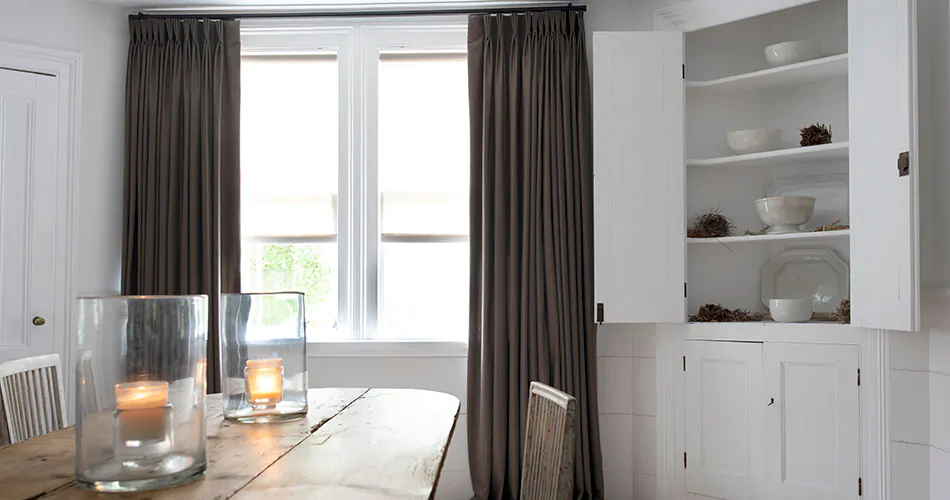 A contemporary dining room shows an example of drapery styles in its dark gray pinch pleat drapes for a transitional style