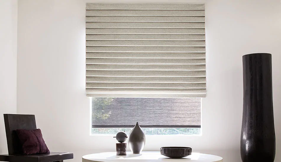 A contemporary room features modern art pieces and a large window covered by Pleated Roman Shades made of Wool Blend Fleece