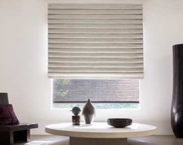 Pleated Roman Shade hung over a Roller Shade on large window with a large white table and large black vase