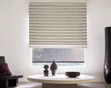 Pleated Roman Shade hung over a Roller Shade on large window with a large white table and large black vase