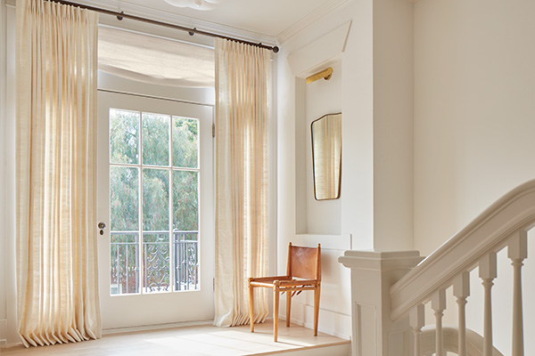 A hallway door features door window coverings with a Relaxed Roman Shade made of Luxe Sheer Linen in Off-White above it and Raw Silk drapery on each side