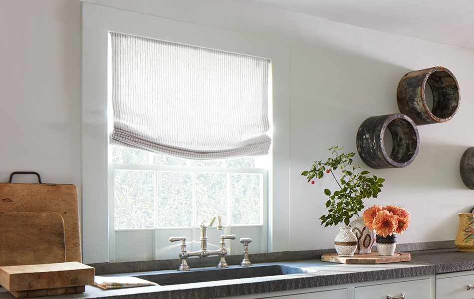 Relaxed linen Roman Shades made of Windsor Stripe in Sage cover windows over a dark granite kitchen counter