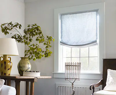 A Relaxed Roman Shade made of Windsor Stripe in Vista lends a coastal feel to a bright sitting room with a large plant
