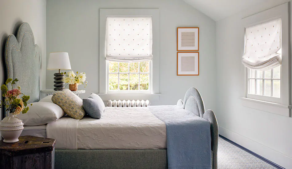 An inviting bedroom with cool colors and an upholstered curved bed frame has Relaxed Roman Shades made of Celeste in Moon