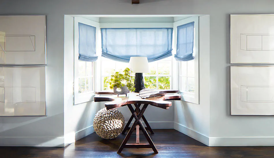 A coastal-style nook has relaxed roman shades made of Holland and Sherry Andes in Fountain instead of bay window curtains