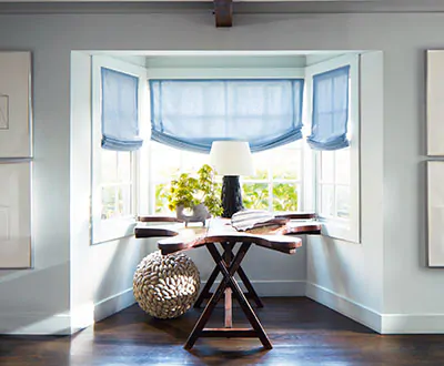 Roman shades for windows include Relaxed Roman Shades made of Andes in Fountain in a bay window with a rustic driftwood table