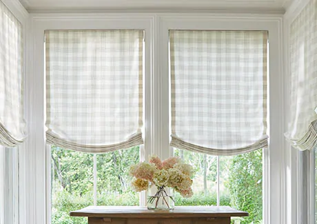 Relaxed Roman Shades made of Emerson in Shea are used as sunroom window treatments in a nook within a sunroom