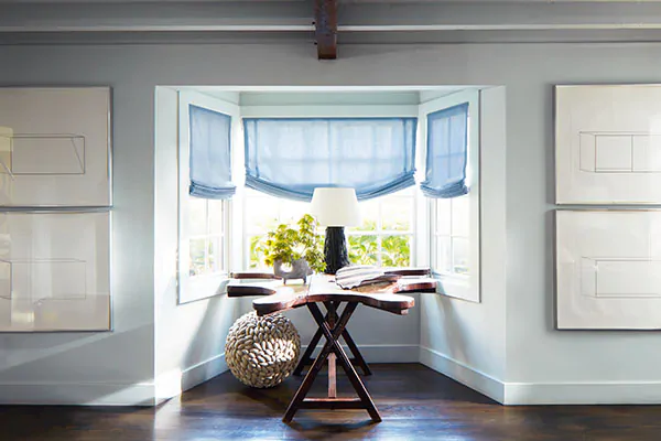 A coastal-inspired nook features a driftwood table and Relaxed Roman Shades made of Andes in Fountain