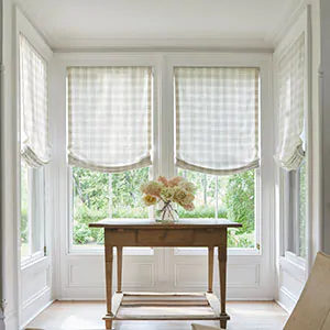 Window treatments for bay windows include Relaxed Roman Shades made of Emerson in Shea in a farmhouse-style nook