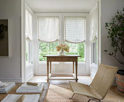 Window treatments for bay windows include Relaxed Roman Shades made of Emerson in Shea in a rustic-inspired box bay window