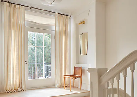 Pinch Pleat Drapery of Raw Silk in Glacier and Relaxed Roman Shades in Luxe Sheer Linen, Off-White adorn a hallway glass door