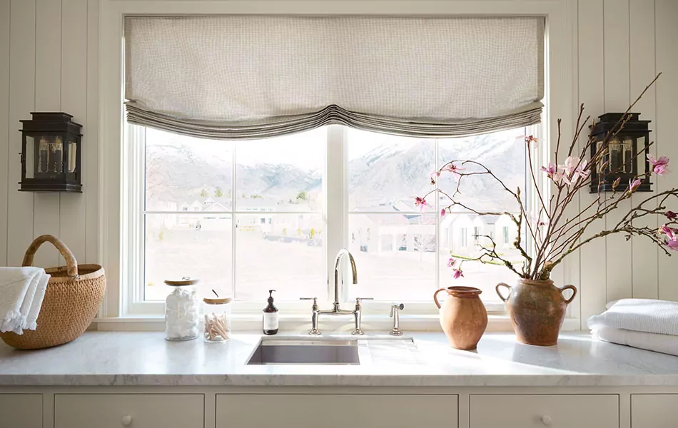 Relaxed Roman Shades made of Galley Gingham in Willow add a charming touch to windows behind a kitchen sink