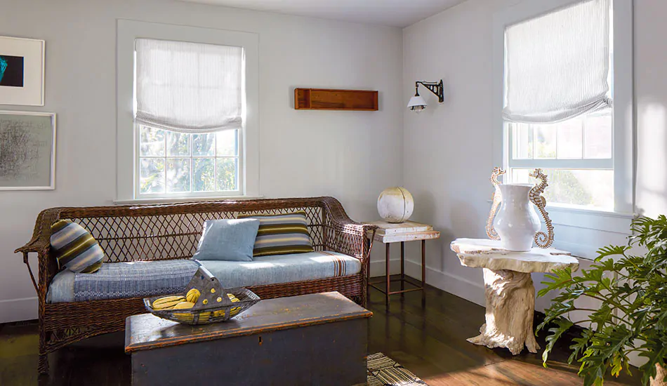 Contemporary window treatments in a coastal inspired sitting room include relaxed roman roman shades with subtle stripes